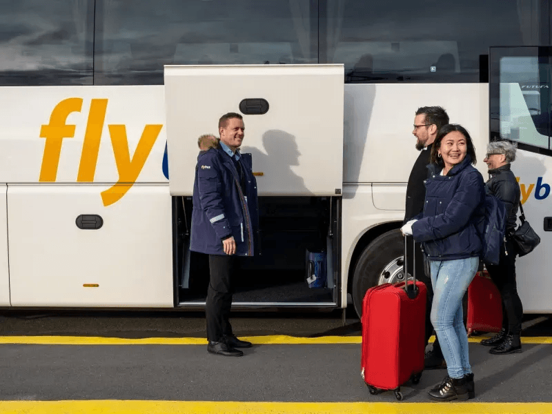 Free Airport Transfer from Keflavik — Pickup & Drop-off Included Smiling travelers with red suitcases boarding an airport shuttle at Keflavik, illustrating free pickup and drop-off for Iceland campervan rentals.