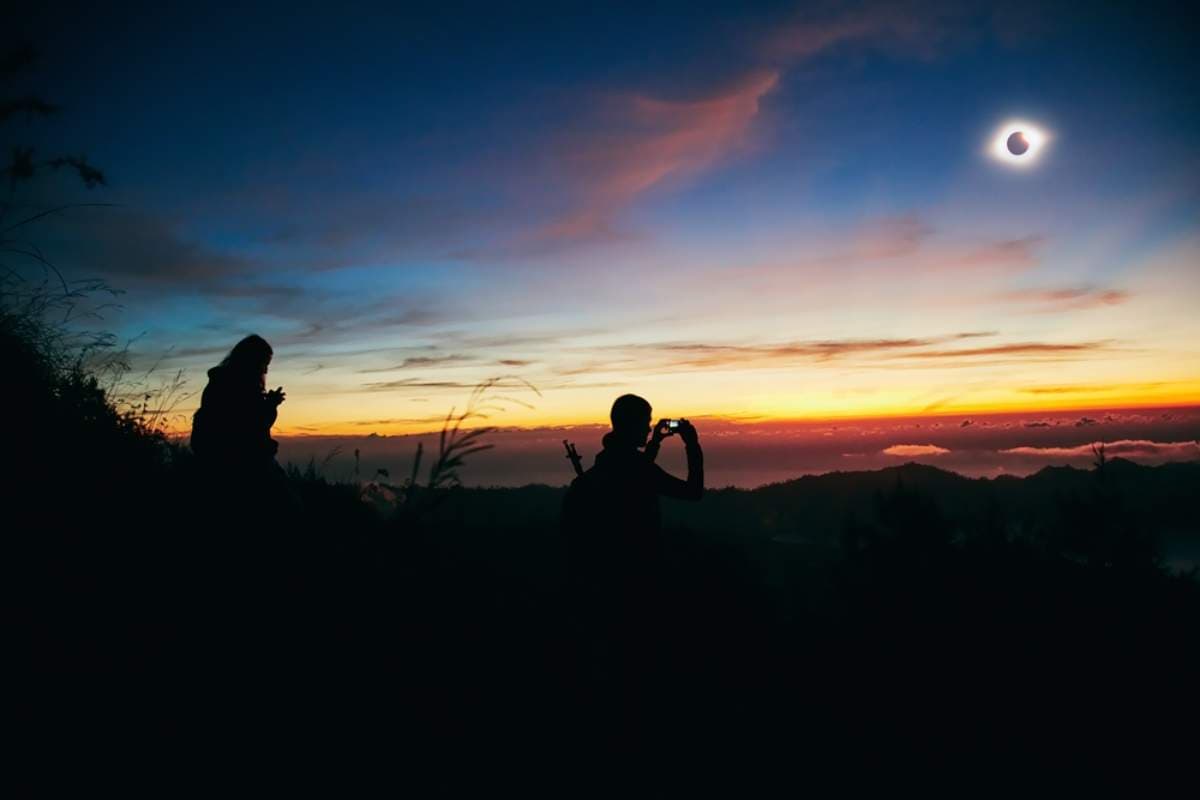 Silhouetted travelers watching a solar eclipse at sunset from a hilltop viewpoint